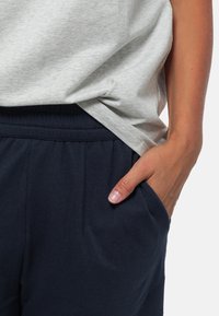 Lichtgrijze melange T-shirt gecombineerd met marineblauwe sweatpants, met een elastische tailleband en zijzakken, getoond tegen een neutrale achtergrond.