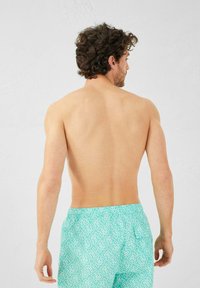 Bañador turquesa con un diseño blanco estampado, cinturilla elástica y un bolsillo trasero, mostrado desde la parte posterior.