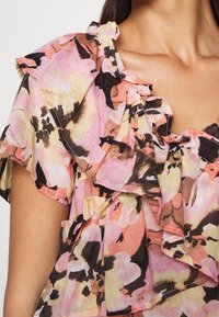 Blomstret bluse med pink, gul og sort mønster. Let, flæset design med korte ærmer og rund halsudskæring.