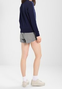 Námornická modrá dlouhá mikroflísová košile v kombinaci se šedými šortkami. Bílé ponožky a světlé tenisky doplňují celkový vzhled. Pohled zezadu.