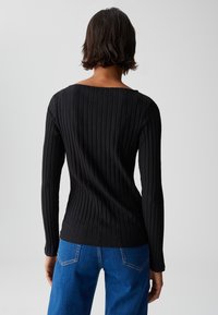 Schwarzes, geripptes Longsleeve-Oberteil mit weitem Halsausschnitt, kontrastiert durch blaue Denim-Jeans, die die Texturen und das figurbetonte Design hervorheben.
