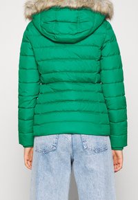 Chaqueta de plumón verde con capucha con borde de piel, diseño acolchado y mangas largas. Combinada con jeans de mezclilla azul claro.
