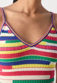 Gros plan sur un débardeur en maille rayée multicolore avec décolleté en V, porté par une personne à la peau brune moyenne.