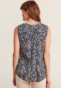 Top senza maniche navy e crema con motivo floreale, collo rotondo e orlo leggermente curvo. Il tessuto sembra leggero e ha una consistenza morbida.