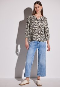 Langærmet v-hals bluse med sort og creme abstrakt mønster; parret med lyseblå brede jeans og hvide sneakers.
