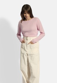 Helles rosa Langarmshirt aus weichem Stoff, kombiniert mit hochgeschnittenen, cremefarbenen Hosen mit Gürtel und vorderen Taschen, frontal präsentiert.