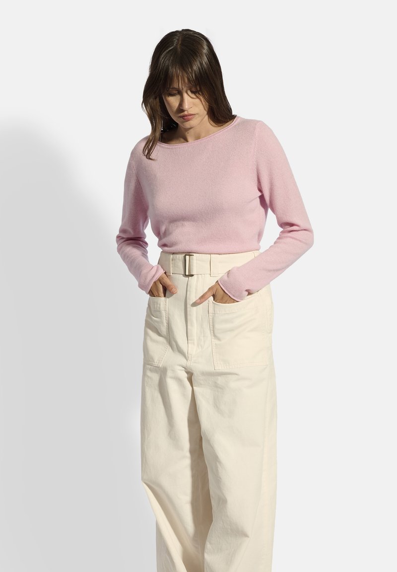 Helles rosa Langarmshirt aus weichem Stoff, kombiniert mit hochgeschnittenen, cremefarbenen Hosen mit Gürtel und vorderen Taschen, frontal präsentiert.