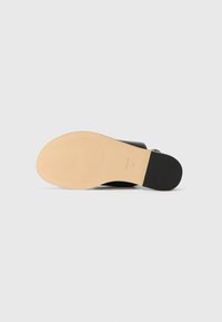 Scarpa nera con parte superiore in pelle liscia, dotata di suola in gomma beige, texture sottile e tacco leggero. Include cuciture tono su tono e una cintura.