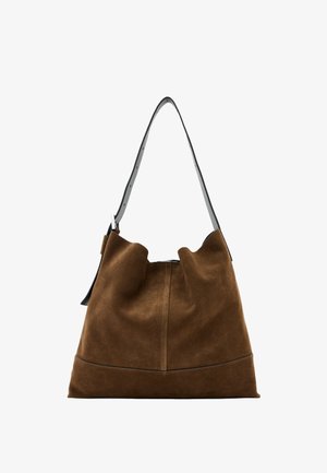 Bruine suede emmer tas met een zwarte leren schouderriem, met een zachte silhouette en naaddetail aan de onderkant.