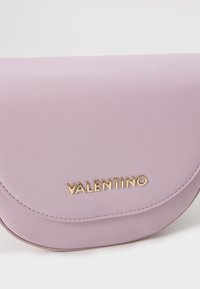 Violeta ādas crossbody soma ar izliekto vāku, ar zeltītu "VALENTINO" logo un izšūtu apdari gar malām.