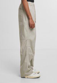Light beige cargo pants with a relaxed fit, elastic waistband, side pockets, and subtle stitching details. Worn with white sneakers.