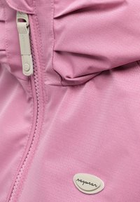 Close-up van roze jasstof met subtiel chevronpatroon, witte rits en klein wit logo-label.