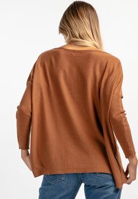 Brązowy, oversize sweter dzianinowy z długimi rękawami, ściągaczami i rozcięciami po bokach. Miękka tekstura i luźny krój, idealny do warstwowego noszenia.