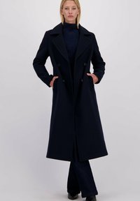 Lang navyblauw wollen jas met een dubbelgeknoopte ontwerp, geknipte kraag en zijzakken, met een getailleerde pasvorm en minimalistische stijl.