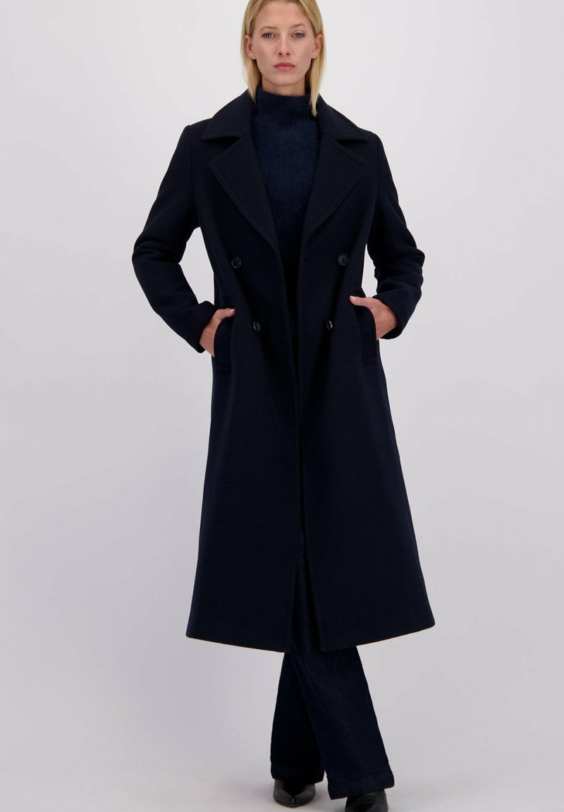 Lang navyblauw wollen jas met een dubbelgeknoopte ontwerp, geknipte kraag en zijzakken, met een getailleerde pasvorm en minimalistische stijl.