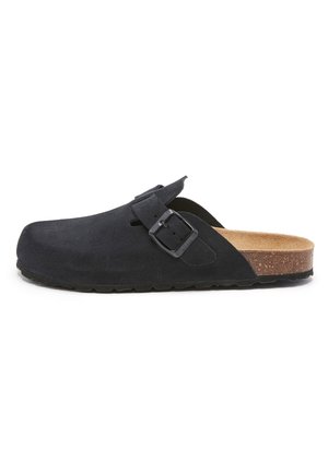Sort ruskind slip-on træsko med justerbar spænde, kork-sål og tekstureret sort gummisål, set fra siden på hvid baggrund.