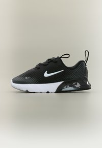 Μαύρο αθλητικό παπούτσι Nike με λευκό λογότυπο swoosh, λευκή σόλα, ταινίες έλξης στη φτέρνα και τη γλώσσα, και επάνω μέρος με σημειωτή υφή, εμφανιζόμενο από το πλάι.