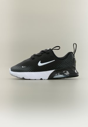 Črni Nike copat z belim logotipom, belim podplatom, zankama na peti in jezičku ter zgornjim delom z teksturo pik, prikazan s strani.