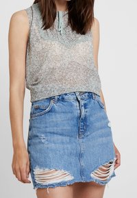 Top sin mangas con estampado floral y un borde de encaje, combinado con una falda de mezclilla desgastada que presenta grandes desgastes y una silueta ajustada.