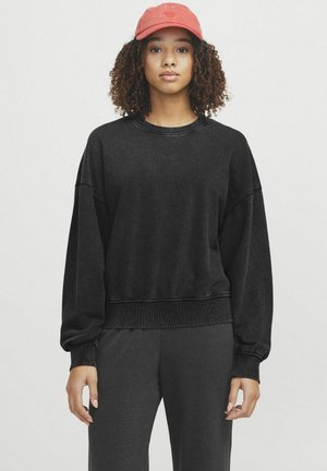 Zwarte katoenen sweatshirt met een losse pasvorm, geribbelde manchetten en zoom. Het model draagt een rode pet en benadrukt een casual, ontspannen stijl.