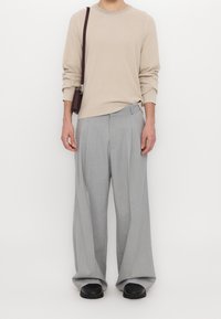 Beżowy sweter na drutach z długimi rękawami, zestawiony z luźnymi, jasnoszarymi spodniami. Dodatki obejmują małą, ciemnobrązową torebkę na ramię.