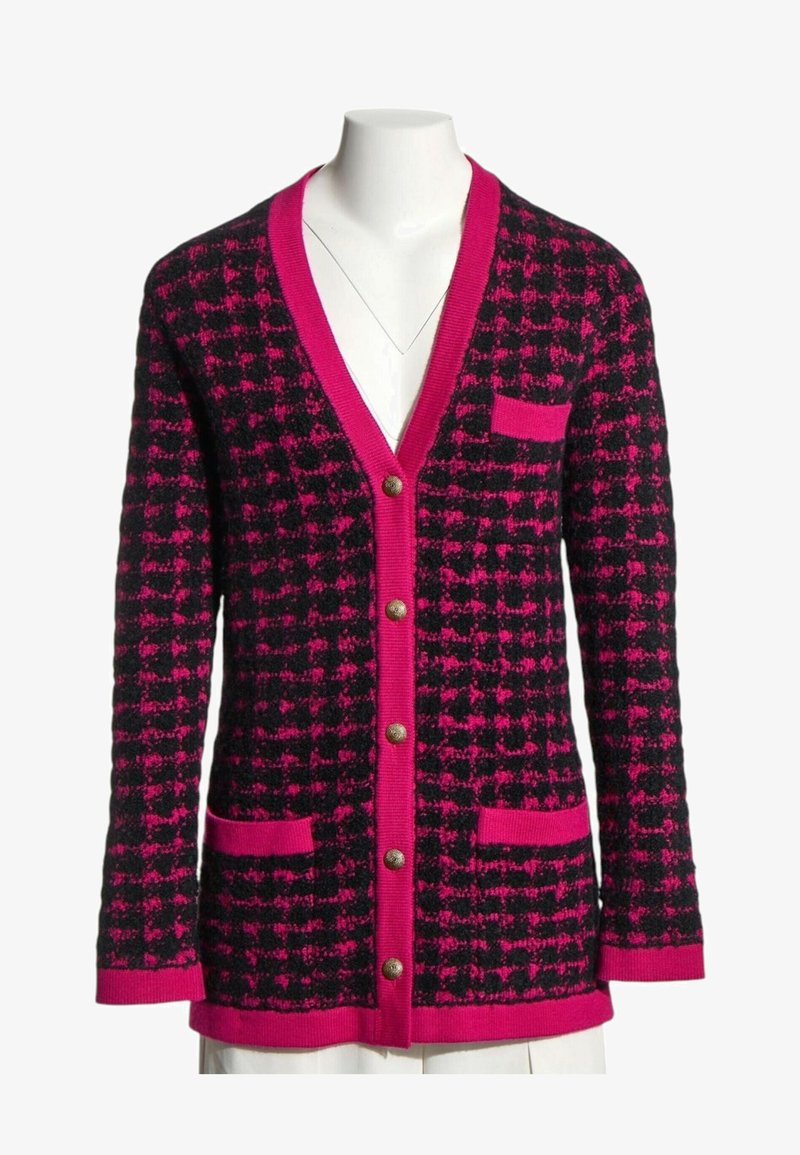 Cardigan en tricot à carreaux noir et rose vif, avec des boutons sur le devant, trois poches et un col en V profond sur un buste de mannequin blanc.
