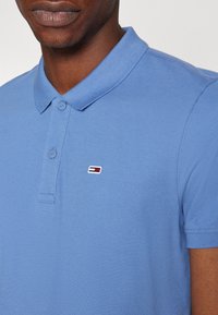 Camisa polo de color azul claro con un tejido texturizado, cuello acanalado, tapeta de botones de dos botones y un pequeño logo bordado en el pecho.