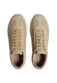 Zapatillas deportivas beige con parte superior sintética suave, punta redonda, diseño de cordones y suela de goma blanca con un branding mínimo.