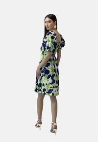 Vestido con estampado floral en colores verde, azul marino y blanco. Mangas abullonadas y diseño de espalda cuadrada. Se combina con tacones blancos y un gran pendiente.