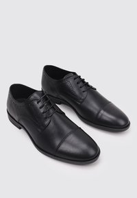 Zapatos de vestir de cuero negro con una textura suave, cierre de cordones, punta redondeada y detalles perforados decorativos a lo largo de los lados.