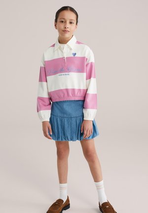 Pulover cu dungi albe și roz, cu guler și text brodat, asortat cu o fustă mini din denim albastru, cu design în straturi. Pantofi maro de tip loafers și șosete albe.