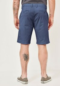 Navy blue shorts made of fabric with a subtle texture, featuring two back pockets and a straight leg cut. Tattoo of a palm tree on the leg.