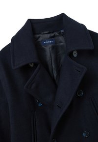 Cappotto in lana blu navy con design doppiopetto, grande colletto, bottoni blu e fodera interna liscia con etichetta visibile.
