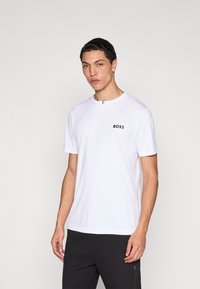 Biele tričko s krátkym rukávom vyrobené z hladkej látky s okrúhlym výstrihom. Na hrudi má čierne logo "BOSS" a prúžkovaný detail.