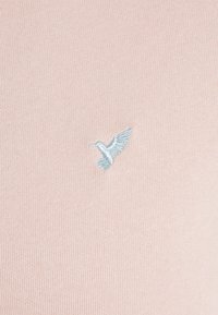 Suéter de punto en rosa claro con un pequeño logotipo de pájaro bordado en azul en el lado izquierdo. Textura suave y diseño ajustado.
