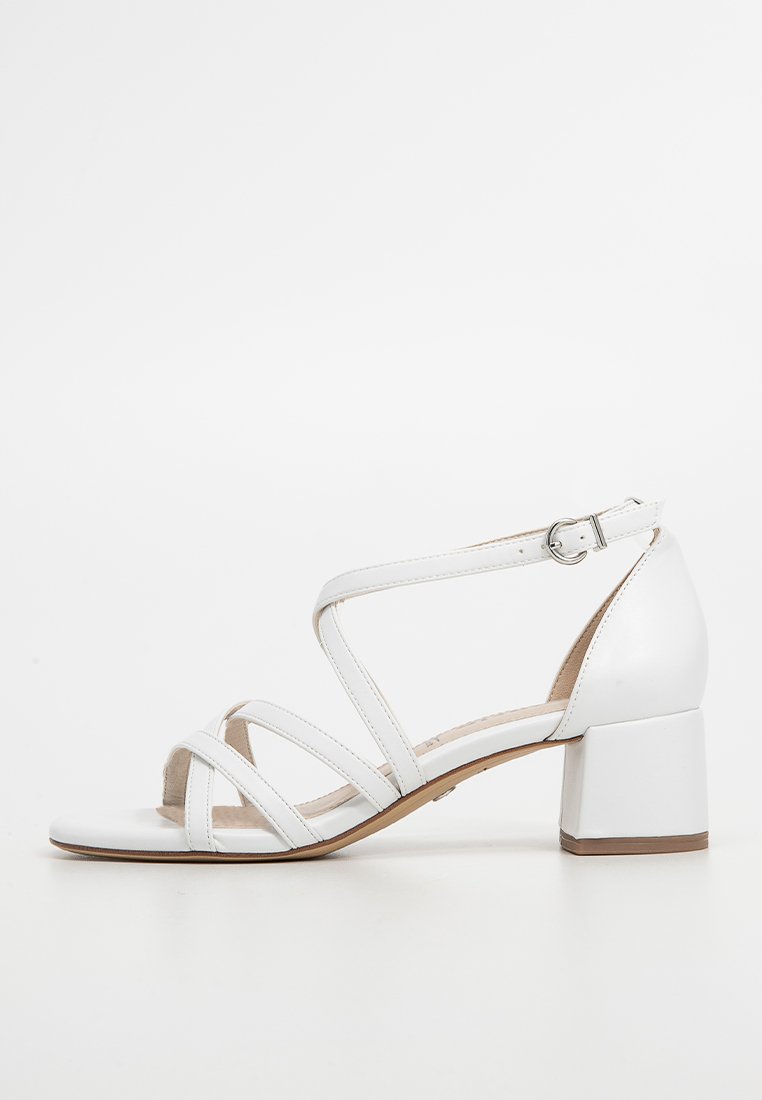 Sandales à talons blancs avec plusieurs lanières entrecroisées, boucle à la cheville et talon épais. Matériau en cuir lisse et semelle beige.