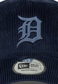 Zils korduroja beisbola vāciņš ar izšūtu baltu "D" logo. Ietver regulējamu siksnu un apļveida "New Era" etiķeti uz malas.