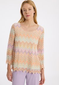 Spitzenoberteil mit einem welligen Chevron-Muster in Pastellfarben: Orange, Lavendel, Minze und Creme. 3/4-Ärmel und ein runder Ausschnitt.