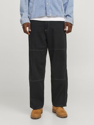 Zwarte wijde broek met contrasterende stiksels, gemaakt van duurzaam materiaal. Combinatie met tan kleurige werkschoenen en een lichtblauwe spijkerjacket.