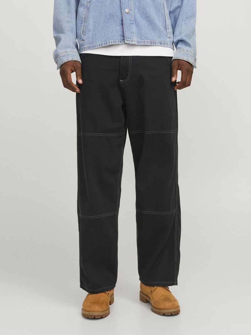 Zwarte wijde broek met contrasterende stiksels, gemaakt van duurzaam materiaal. Combinatie met tan kleurige werkschoenen en een lichtblauwe spijkerjacket.