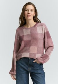 Maglione all'uncinetto in un motivo a quadri bordeaux e rosa, con colletto rotondo e maniche lunghe, abbinato a jeans blu scuro.