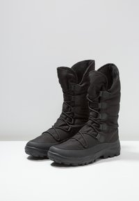 Botas negras de nieve con parte superior de tela texturizada, correas ajustables y suelas de goma para tracción. Presentan una caña alta y forro aislante.