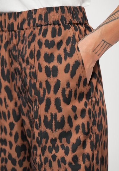 Pruun leopardimustriga püksid on varustatud elastse vöökoha ja taskutega, valmistatud sujuvast ja tekstuurilisest kangast. Muster on julge ja kontrastne.