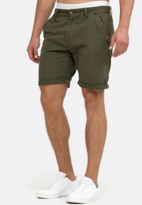 Shorts en coton vert olive avec revers roulés, poches avant et fermeture par bouton. Associés à des baskets blanches pour un look décontracté.