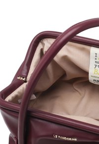 Borsa color bordeaux con esterno in pelle liscia, fodera in tessuto beige e dettagli in metallo dorato. Contiene un'etichetta per la cura all'interno.