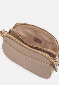 Beige lædertaske til at bære over kroppen med en tekstureret overflade, to lynlåsområder, guldfarvet hardware og en foring af stof indvendigt.