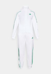 Valkoinen urheiluasu, joka on valmistettu sileästä kankaasta. Siinä on vihreät sivu raidat, vetoketjullinen takki ja joustavat hihnat housuissa. Adidas-logo takissa.
