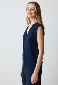 Top senza maniche di un blu navy con un profondo scollo a V, texture liscia e silhouette aderente, abbinato a pantaloni coordinati.