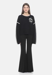 Schwarzer Strickpullover mit weißen Streifen an den Ärmeln und gesticktem Design; kombiniert mit schwarzen Schlaghosen; lässige Passform.