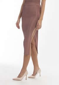 Knielanger Bleistiftrock aus schimmerndem roségoldenen Stoff, mit einem hohen Schlitzdetail. Kombiniert mit blassrosa High Heels.